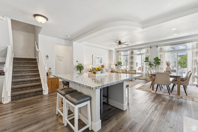 1076 S Meadow Walk Ln, Heber City, UT 84032 - kitchen with a textured ceiling, a breakfast bar area, dark wood-style floors, light stone countertops, and a center island