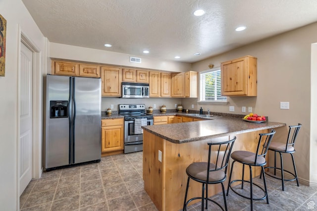 52 N 1100 W, Springville, UT 84663 - kitchen with appliances with stainless steel finishes, a peninsula, a textured ceiling, dark countertops, and a breakfast bar