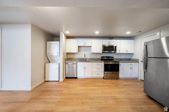 5726 S Highland Dr E, Holladay, UT 84121 - kitchen with stainless steel appliances, stacked washer and clothes dryer, white cabinetry, dark stone counters, and recessed lighting
