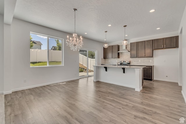 2123 N Wallflower Dr, Saratoga Springs, UT 84045 - kitchen with wall chimney range hood, tasteful backsplash, recessed lighting, dark brown cabinets, and light countertops