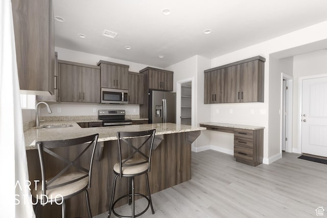 668 E Fiddlers Cove Dr Unit 35, Cedar City, UT 84721 - kitchen with appliances with stainless steel finishes, a peninsula, light wood-style flooring, a kitchen breakfast bar, and light stone countertops