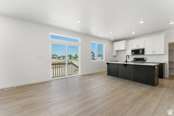 737 N Plainsman Dr Unit 108, Spanish Fork, UT 84660 - kitchen featuring stainless steel microwave, stove, light countertops, light wood-style flooring, and a center island with sink