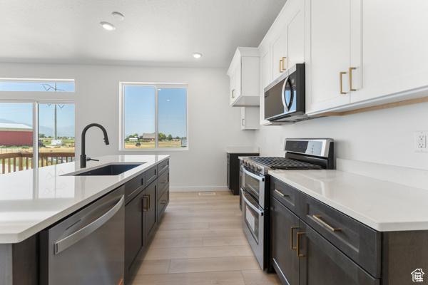 737 N Plainsman Dr Unit 108, Spanish Fork, UT 84660 - kitchen with appliances with stainless steel finishes, white cabinets, light wood-style flooring, light countertops, and a center island with sink