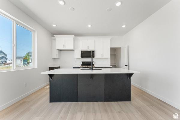 737 N Plainsman Dr Unit 108, Spanish Fork, UT 84660 - kitchen featuring stainless steel microwave, light wood finished floors, white cabinetry, a center island with sink, and recessed lighting