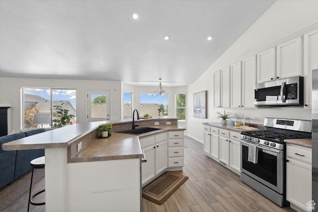 6515 S Mount Whitney Ln, West Valley City, UT 84118 - kitchen featuring appliances with stainless steel finishes, lofted ceiling, a breakfast bar area, white cabinetry, and a kitchen island with sink