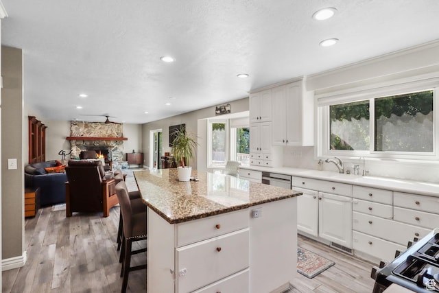 9618 S Ruskin Cir E, Sandy, UT 84092 - kitchen featuring a center island, light wood-style flooring, recessed lighting, a stone fireplace, and light stone counters
