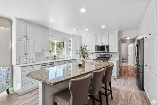 9618 S Ruskin Cir E, Sandy, UT 84092 - kitchen with stainless steel appliances, light wood-style floors, a kitchen bar, a kitchen island, and white cabinetry