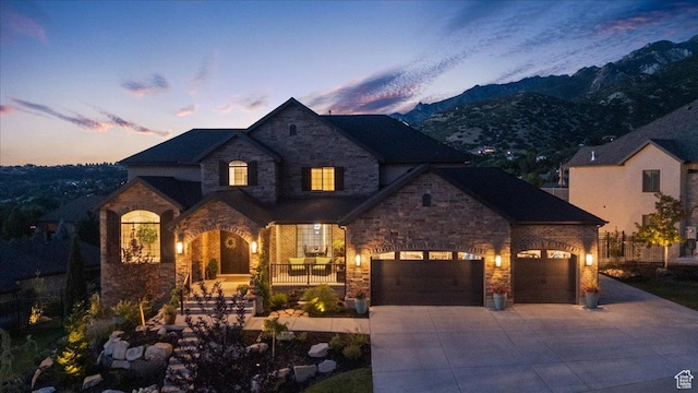 10865 S Hiddenwood Dr, Sandy, UT 84092 - french country style house with stone siding, concrete driveway, a mountain view, a porch, and an attached garage