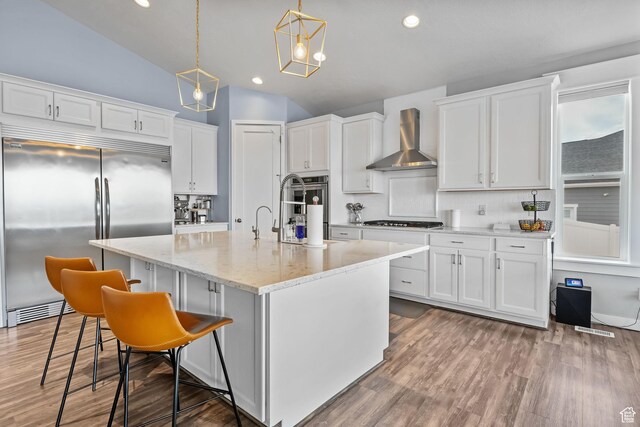 7603 S Scenic Maple Dr S, West Jordan, UT 84081 - kitchen with stainless steel appliances, wall chimney range hood, white cabinets, hanging light fixtures, and vaulted ceiling