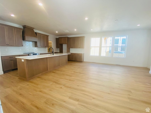 6511 W Lake Ave, South Jordan, UT 84009 - kitchen featuring premium range hood, an island with sink, backsplash, light wood-type flooring, and recessed lighting