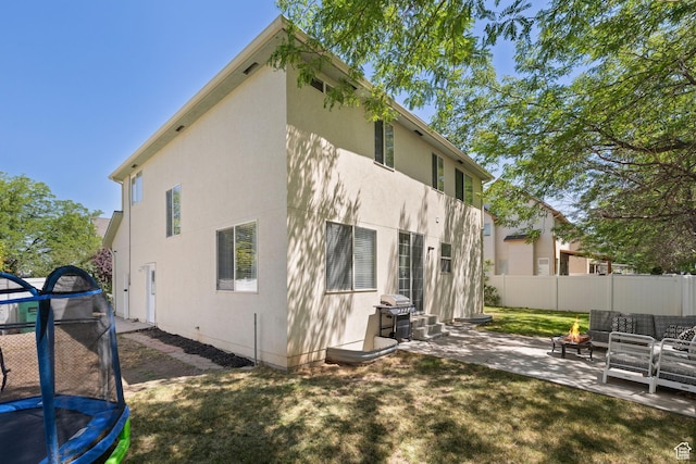 3584 S Autumn Gate Ct, Magna, UT 84044 - rear view of house featuring a trampoline, a patio, stucco siding, and an outdoor living space with a fire pit