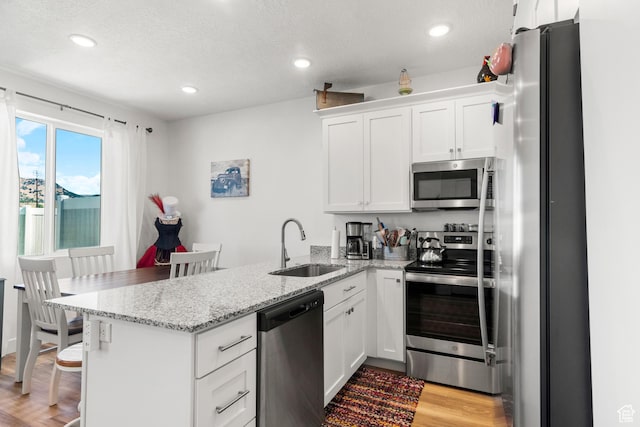 48 E Cedar Ln, Malad City, ID 83252 - kitchen with stainless steel appliances, a peninsula, white cabinetry, light wood-style floors, and light stone counters