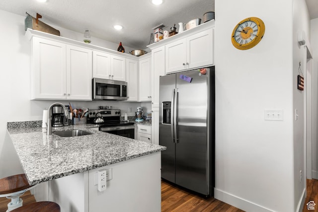 48 E Cedar Ln, Malad City, ID 83252 - kitchen with appliances with stainless steel finishes, a peninsula, a kitchen bar, dark wood-type flooring, and white cabinets