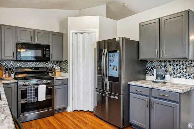 232 Sunstone Cir W, Logan, UT 84321 - kitchen featuring appliances with stainless steel finishes, gray cabinets, light wood-type flooring, decorative backsplash, and vaulted ceiling