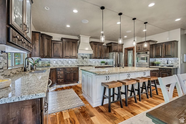 789 Eliza Ct, Farmington, UT 84025 - kitchen featuring custom range hood, appliances with stainless steel finishes, tasteful backsplash, an island with sink, and dark brown cabinets