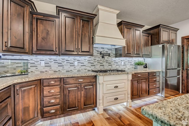 789 Eliza Ct, Farmington, UT 84025 - kitchen with stainless steel appliances, light wood-style flooring, custom range hood, dark brown cabinetry, and tasteful backsplash