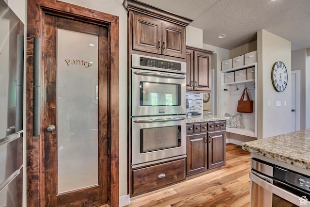 789 Eliza Ct, Farmington, UT 84025 - kitchen featuring stainless steel double oven, light wood-type flooring, light stone countertops, a textured ceiling, and dark brown cabinetry