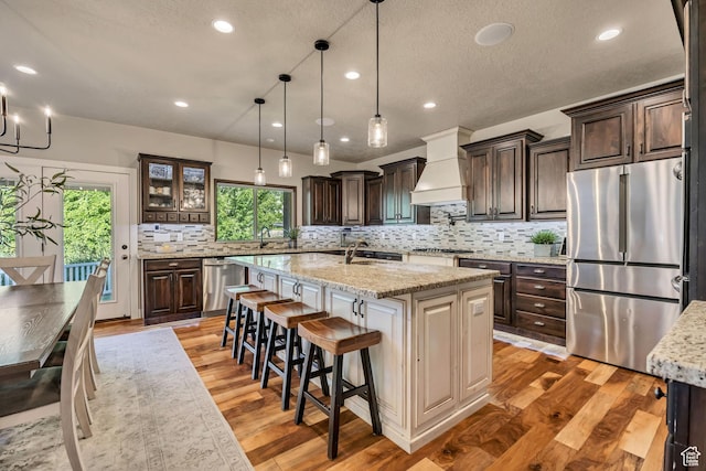 789 Eliza Ct, Farmington, UT 84025 - kitchen with appliances with stainless steel finishes, custom range hood, plenty of natural light, a kitchen island with sink, and a textured ceiling