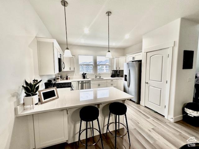4542 Parkes Peak Ln, Riverton, UT 84096 - kitchen featuring appliances with stainless steel finishes, a peninsula, light wood-style flooring, white cabinetry, and pendant lighting