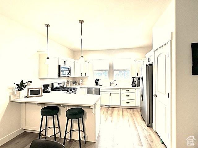4542 Parkes Peak Ln, Riverton, UT 84096 - kitchen featuring stainless steel appliances, a peninsula, light wood-style floors, a kitchen bar, and white cabinetry