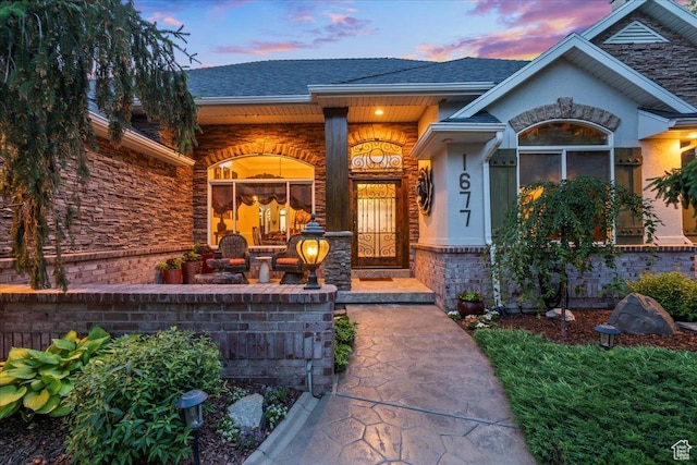 1677 E Wylie Ln, Draper, UT 84020 - exterior entry at dusk featuring a porch, stucco siding, and roof with shingles