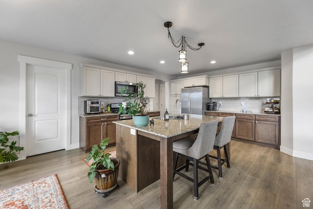 499 N Stone Ridge Dr, Saratoga Springs, UT 84045 - kitchen featuring stainless steel appliances, recessed lighting, light wood finished floors, decorative backsplash, and light stone countertops