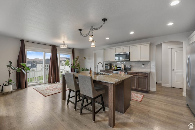 499 N Stone Ridge Dr, Saratoga Springs, UT 84045 - kitchen featuring appliances with stainless steel finishes, light wood-style floors, arched walkways, a kitchen bar, and a center island with sink