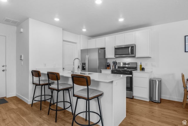 943 E Drifter Ln, Saratoga Springs, UT 84045 - kitchen with stainless steel appliances, a breakfast bar, light wood finished floors, white cabinets, and light countertops