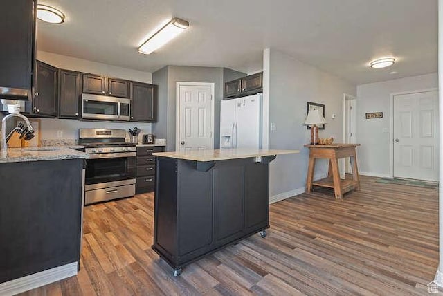 7526 S Park Maple Dr, West Jordan, UT 84081 - kitchen with appliances with stainless steel finishes, wood finished floors, a breakfast bar area, a center island, and dark brown cabinetry