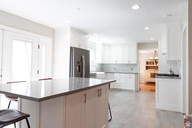 11089 S Justin Dr, Sandy, UT 84092 - kitchen featuring stainless steel fridge, a kitchen bar, white cabinetry, tasteful backsplash, and a kitchen island