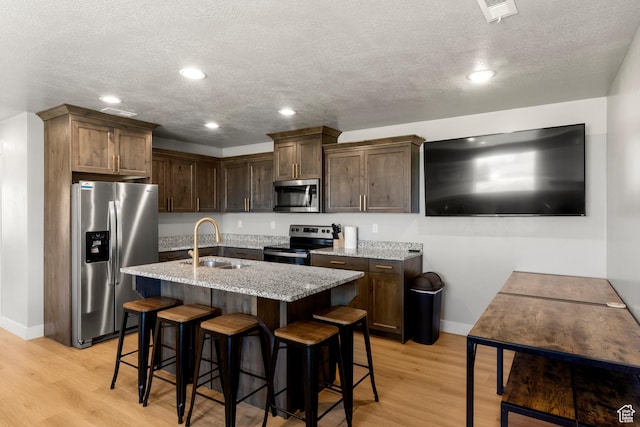 130 W Seasons Loop Upper, Upper, Garden City, UT 84028 - kitchen featuring stainless steel appliances, light stone countertops, light wood-style flooring, a textured ceiling, and a breakfast bar area