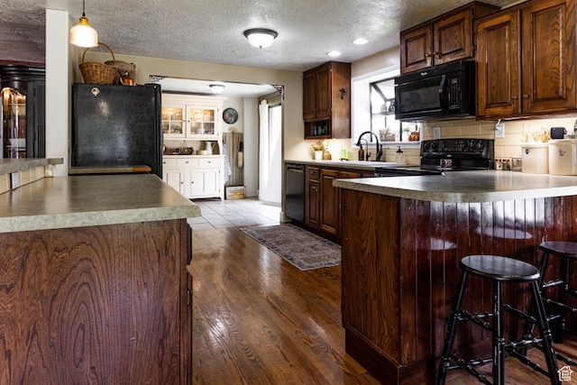 453 Sheridan Cir, Centerville, UT 84014 - kitchen featuring black appliances, a peninsula, a textured ceiling, dark wood-type flooring, and a kitchen bar