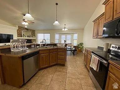 3462 Heyward Ct, Eagle Mountain, UT 84043 - kitchen featuring appliances with stainless steel finishes, dark countertops, vaulted ceiling, plenty of natural light, and brown cabinets