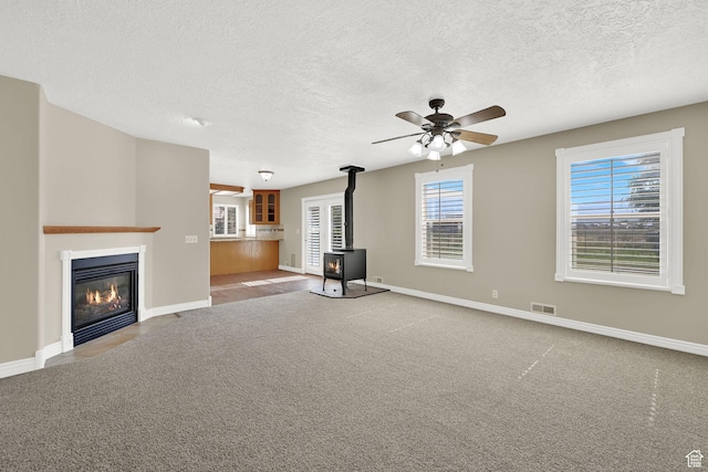 3112 N Pelican Dr, Farr West, UT 84404 - unfurnished living room featuring a wood stove, a ceiling fan, a textured ceiling, a fireplace with flush hearth, and carpet flooring