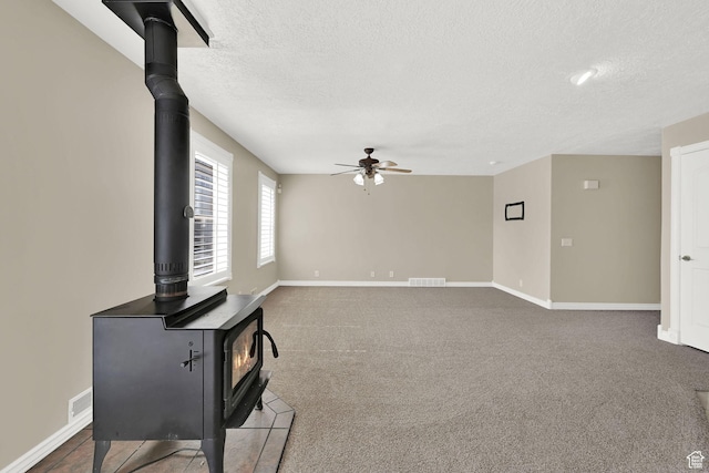 3112 N Pelican Dr, Farr West, UT 84404 - unfurnished living room featuring a wood stove, a textured ceiling, ceiling fan, and carpet flooring