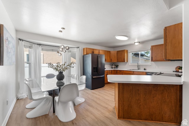 4974 W Diamondback Dr, Riverton, UT 84096 - kitchen featuring refrigerator with ice dispenser, brown cabinetry, light countertops, light wood finished floors, and a peninsula