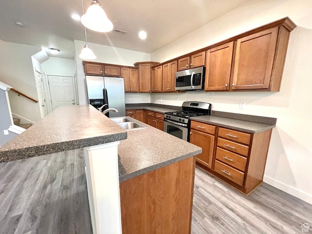 3794 W Angelica Ct, South Jordan, UT 84095 - kitchen featuring stainless steel appliances, brown cabinetry, a kitchen island with sink, light wood-style flooring, and dark countertops