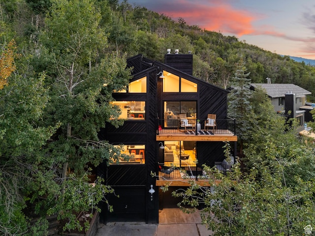 947 Northstar Dr, Park City, UT 84060 - back of property at dusk featuring a balcony, a chimney, a view of trees, concrete driveway, and a garage