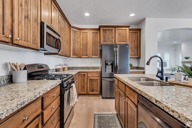 10741 S Topview Rd, South Jordan, UT 84095 - kitchen featuring stainless steel appliances, brown cabinets, arched walkways, light wood-style flooring, and light stone countertops