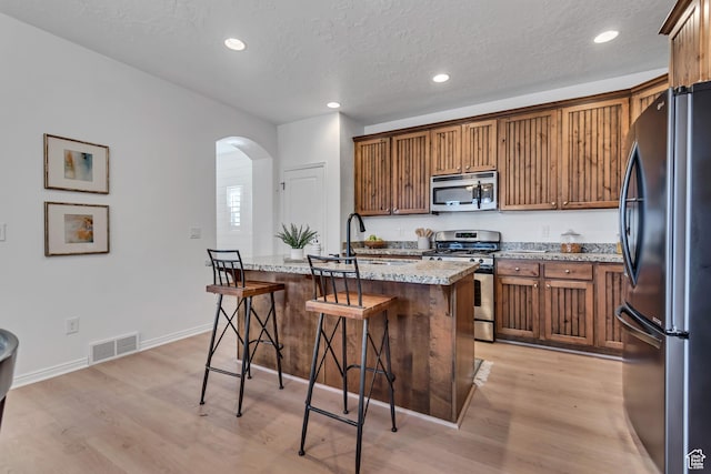 10741 S Topview Rd, South Jordan, UT 84095 - kitchen with stainless steel appliances, arched walkways, light wood-type flooring, a breakfast bar area, and recessed lighting
