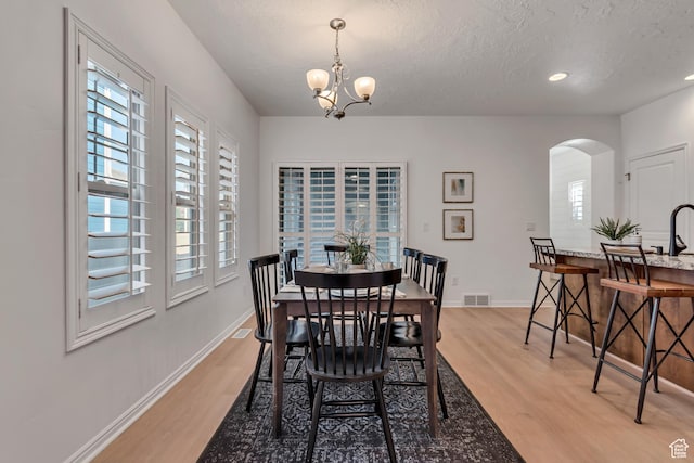 10741 S Topview Rd, South Jordan, UT 84095 - dining space with arched walkways, light wood-type flooring, a chandelier, and a textured ceiling
