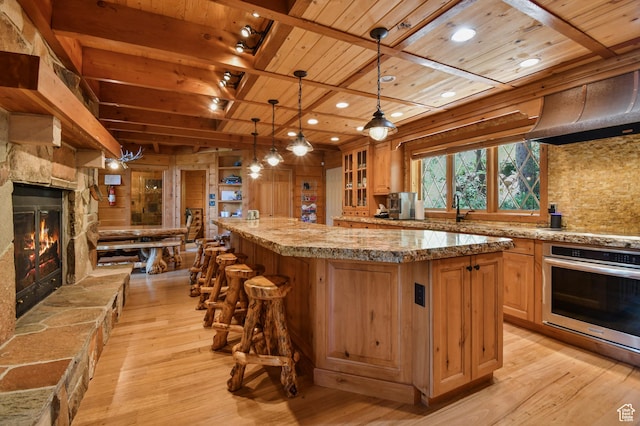 8581 Shingle Mill Dr, Oakley, UT 84055 - kitchen with oven, a wooden ceiling with exposed beams, light wood-type flooring, a center island, and a stone fireplace
