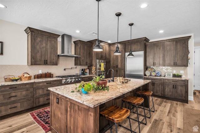 2751 S 3970 W, Hurricane, UT 84737 - kitchen with wall chimney range hood, appliances with stainless steel finishes, decorative backsplash, a breakfast bar, and dark brown cabinets