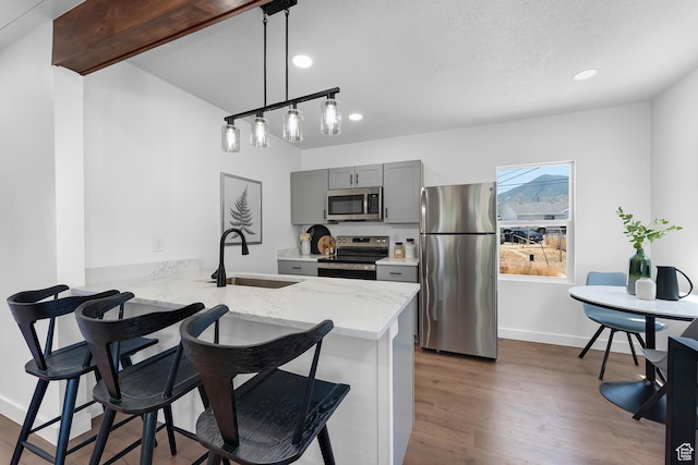 482 N Brook Ave E, Tooele, UT 84074 - kitchen featuring appliances with stainless steel finishes, gray cabinetry, a breakfast bar area, a peninsula, and light stone counters