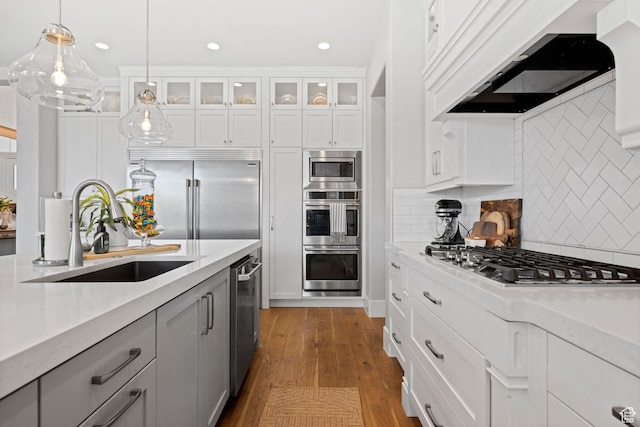 2918 E Willow Tree Ln, St George, UT 84790 - kitchen with built in appliances, range hood, hanging light fixtures, glass insert cabinets, and white cabinets