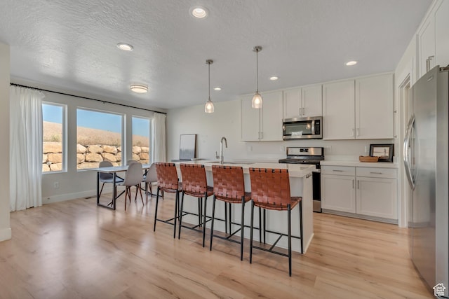 9728 N Aaron Ave Unit 115, Eagle Mountain, UT 84005 - kitchen with appliances with stainless steel finishes, light wood finished floors, white cabinets, a kitchen bar, and recessed lighting