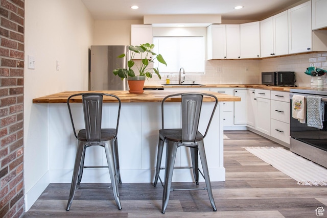 129 N 100 E, Ephraim, UT 84627 - kitchen featuring butcher block countertops, stainless steel appliances, a breakfast bar, white cabinets, and decorative backsplash