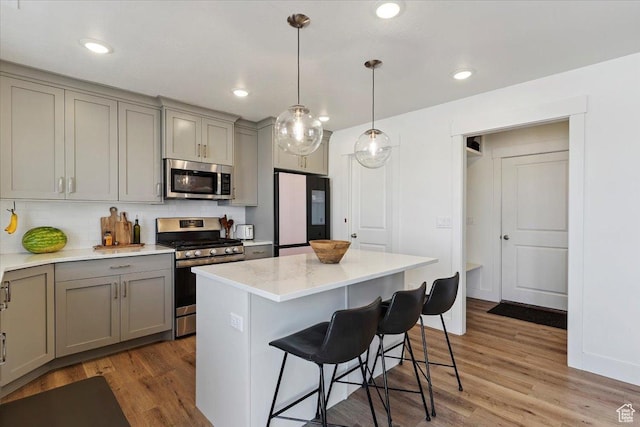 3380 W 3275 N, Plain City, UT 84404 - kitchen with stainless steel appliances, gray cabinets, a kitchen breakfast bar, light wood-type flooring, and backsplash