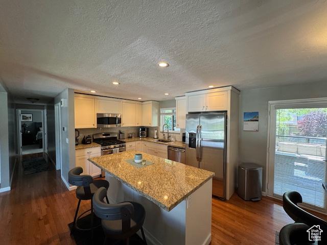 4650 S Chapel Dr E, Salt Lake City, UT 84117 - kitchen with stainless steel appliances, a textured ceiling, dark wood finished floors, a kitchen island, and white cabinets