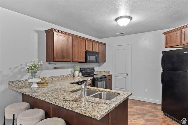 491 S Freedom Blvd Unit 104204, Provo, UT 84601 - kitchen featuring black appliances, a peninsula, a kitchen breakfast bar, light stone counters, and dark wood finished floors